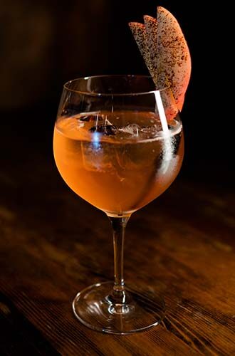 Brown Spiced whiskey cocktail in wine glass sitting on table with dried apple garnish - Redemption Whiskey