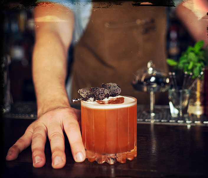 Bartender serving red orange Marooned at Sea whiskey cocktail with ice and fig garnish - Redemption Whiskey