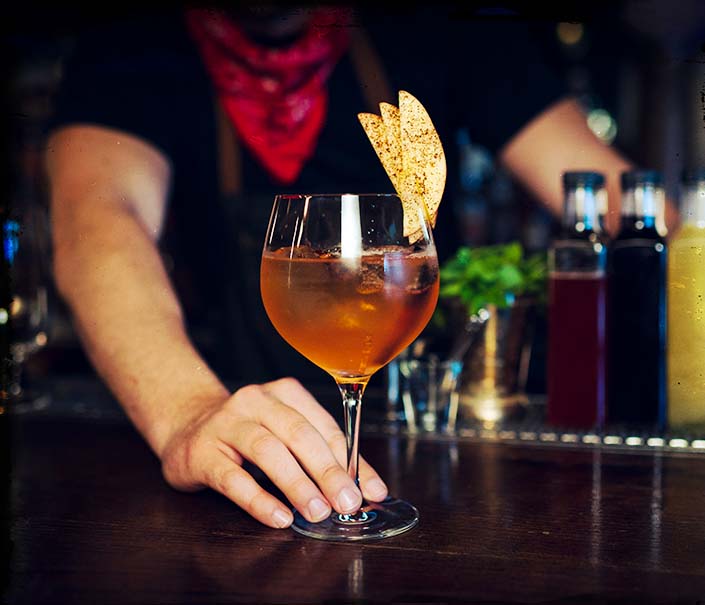 Bartender in red bandana serving brown spiced whiskey cocktail with ice in wine glass and garnish - Redemption Whiskey